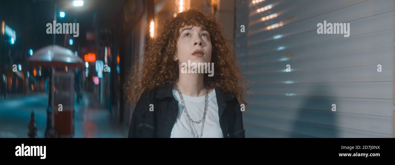 Young woman with curly hair in white t-shirt and black jacket is walking on the street at night, fashion clothing and feminism concept Stock Photo