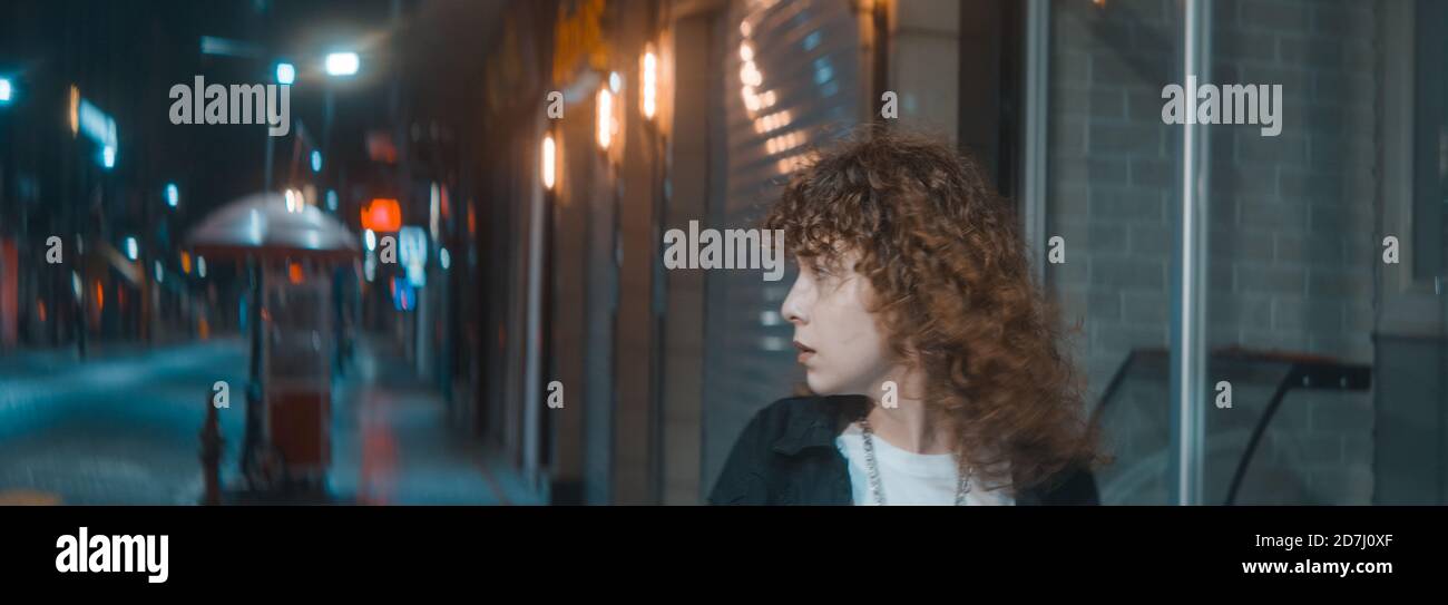 Stressful unhappy young attractive woman with curly hair in white t-shirt and black jacket is walking on the street at the night, fashion clothing and Stock Photo