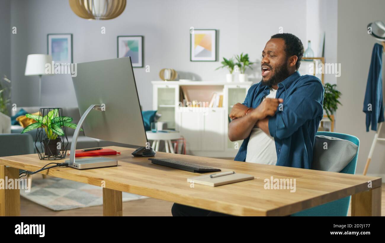 Portrait of the Shocked Handsome African American Man Sitting at His Workplace. Young Man Watching Screamers at Home. Stock Photo