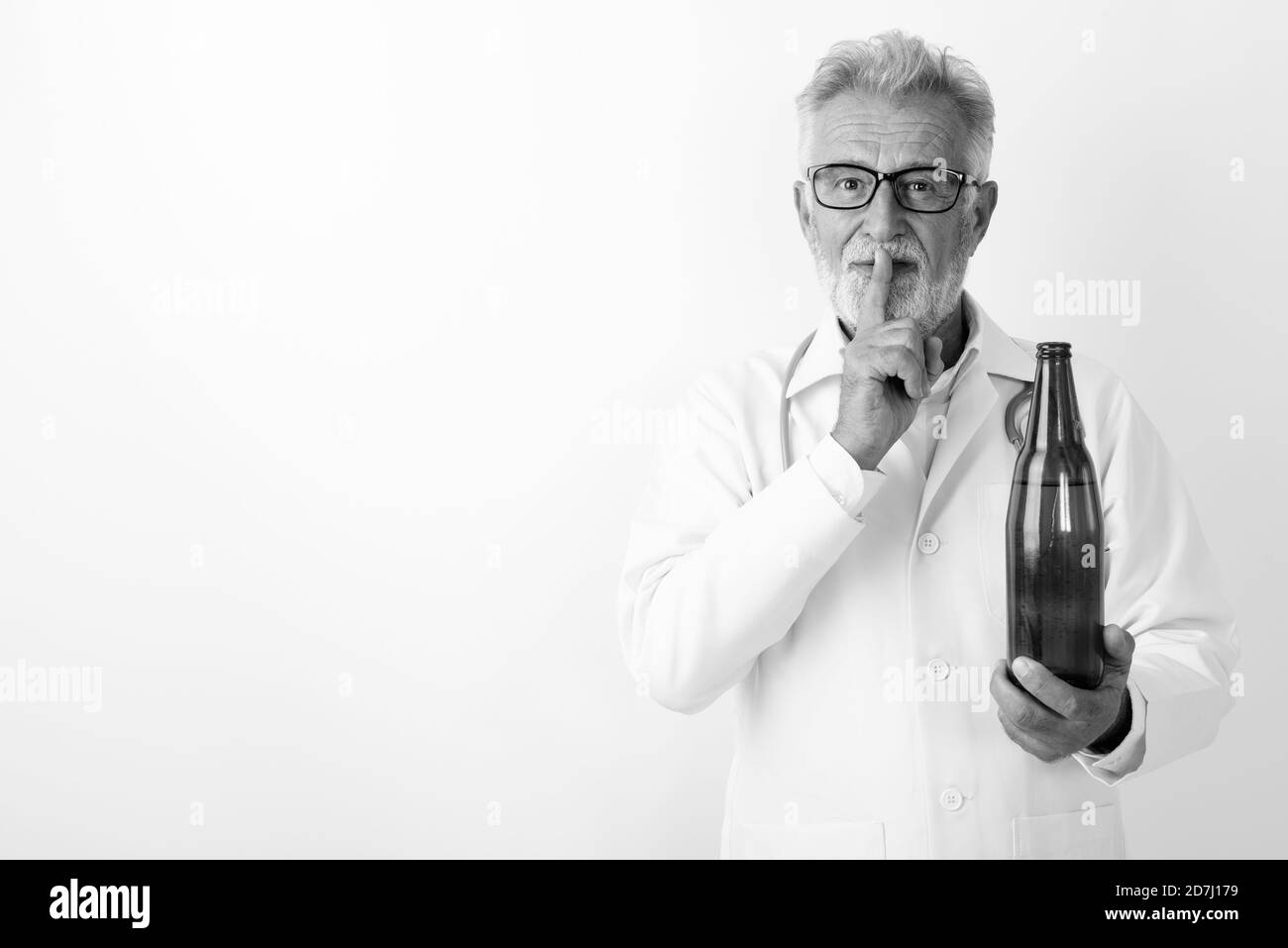Studio shot of handsome senior bearded man doctor holding bottle of beer with finger on lips against white background Stock Photo