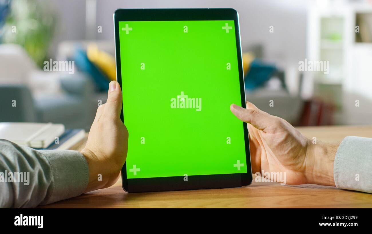 Close-up of a Man's Hand Holding Green Mock-up Screen Smartphone. Modern Mobile Phone. In the Background Cozy Living Room or Home Office. Stock Photo