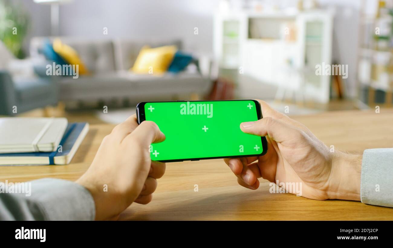 First Person Close-up of the Man Holding Green Screen Smartphone in Landscape Mode and Playing Game with His Thumbs. Stock Photo