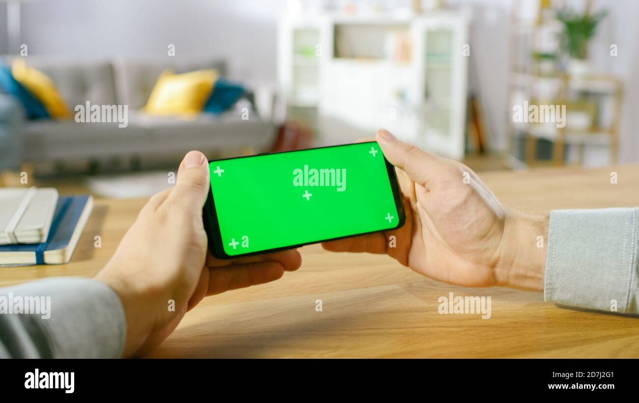 First Person Close-up of the Man Holding Green Screen Smartphone in Landscape Mode and Playing Game with His Thumbs. Stock Photo