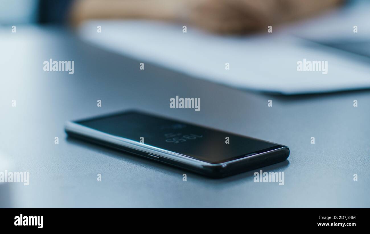 Close-up Shot of the Last Model Smartphone Lying in Office Desk. Focus on a Phone. Stock Photo