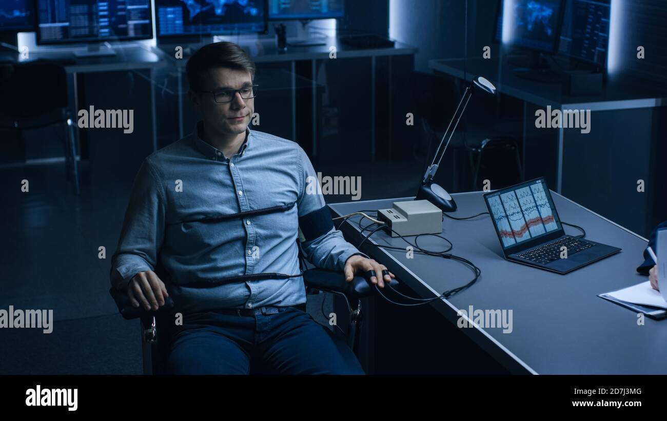 Young Handsome Suspect During Interrogation Undergoes Lie Detector Polygraph Test, Connected to the Machine He Answers Yer or No Questions Which Stock Photo