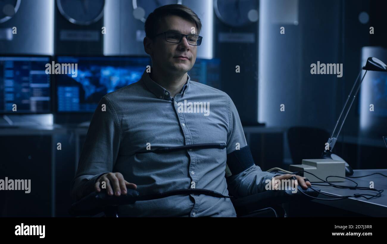 Young Handsome Suspect During Interrogation Undergoes Lie Detector Polygraph Test, Connected to the Machine He Answers Yer or No Questions Which Stock Photo