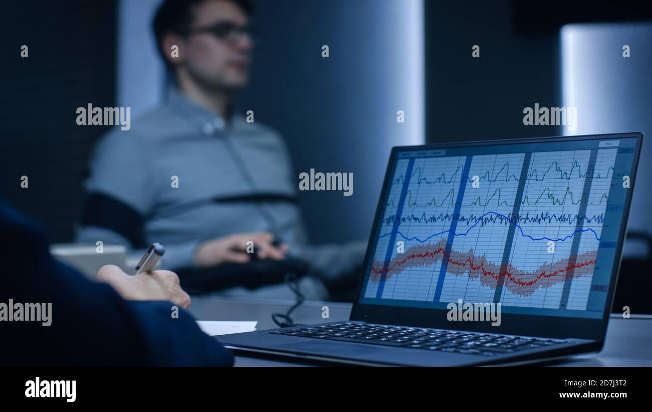 Computer Shows Physiological Measures of a Man Undergoing Lie Detector Polygraph Test. Examining Expert Writes Down Observations.  Stock Photo