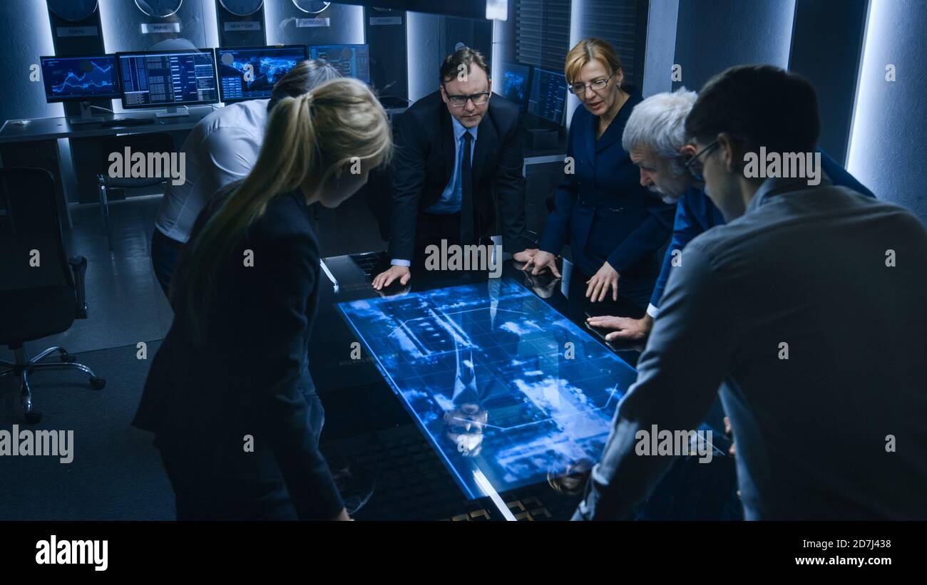 Team of Government Intelligence FBI Agents Standing Around Digital Touch Screen Table and Tracking Suspect Vehicle Using Satellite Surveillance in the Stock Photo