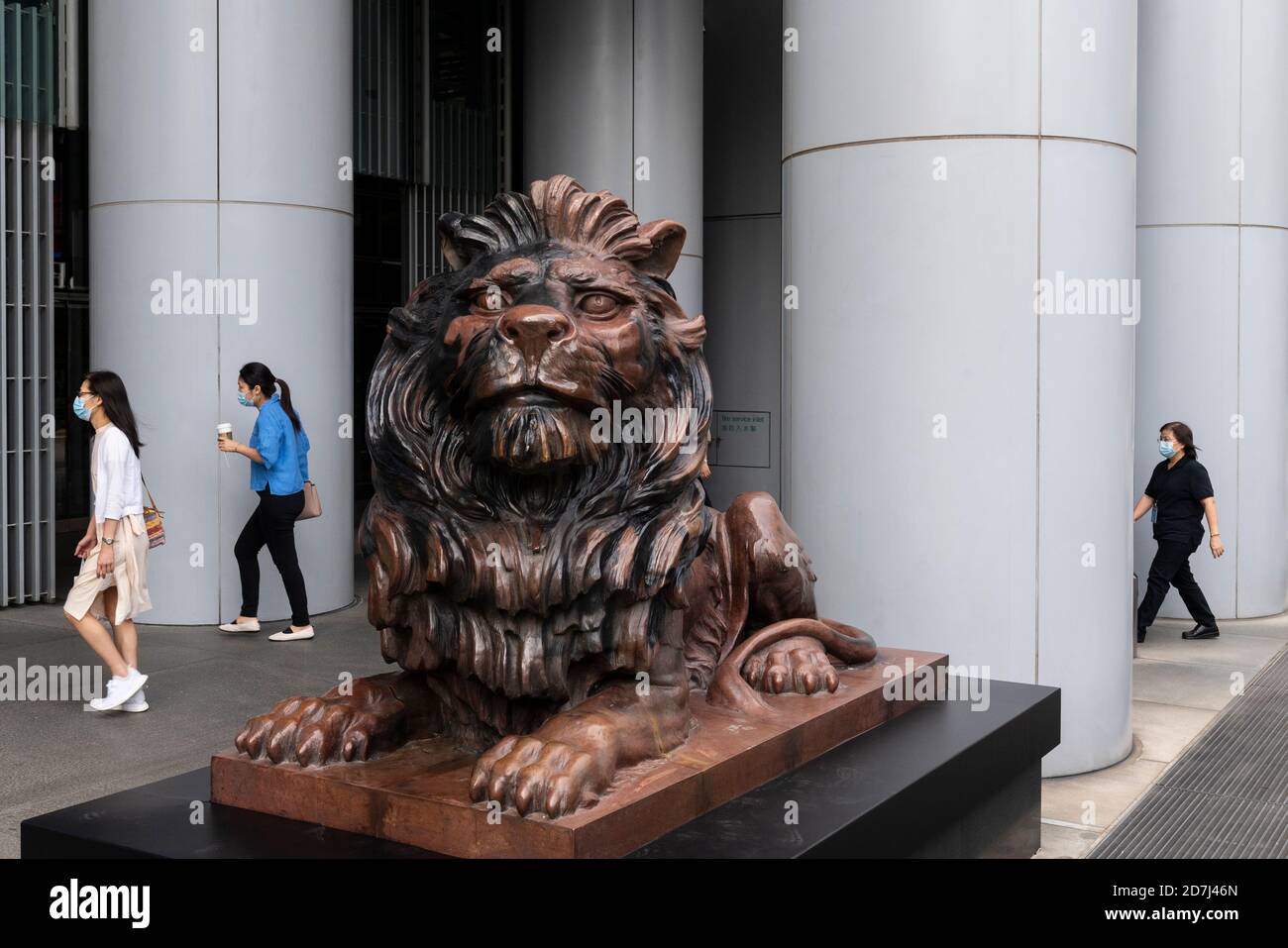 People walk past a bronze lion statue, restored after prodemocracy