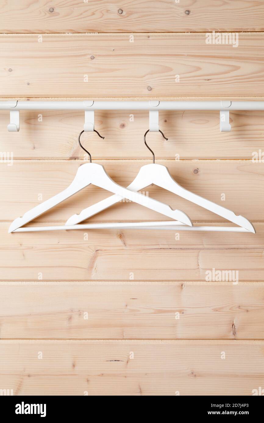 Two white hangers are on hooks near blank wooden wall, vertical background photo Stock Photo
