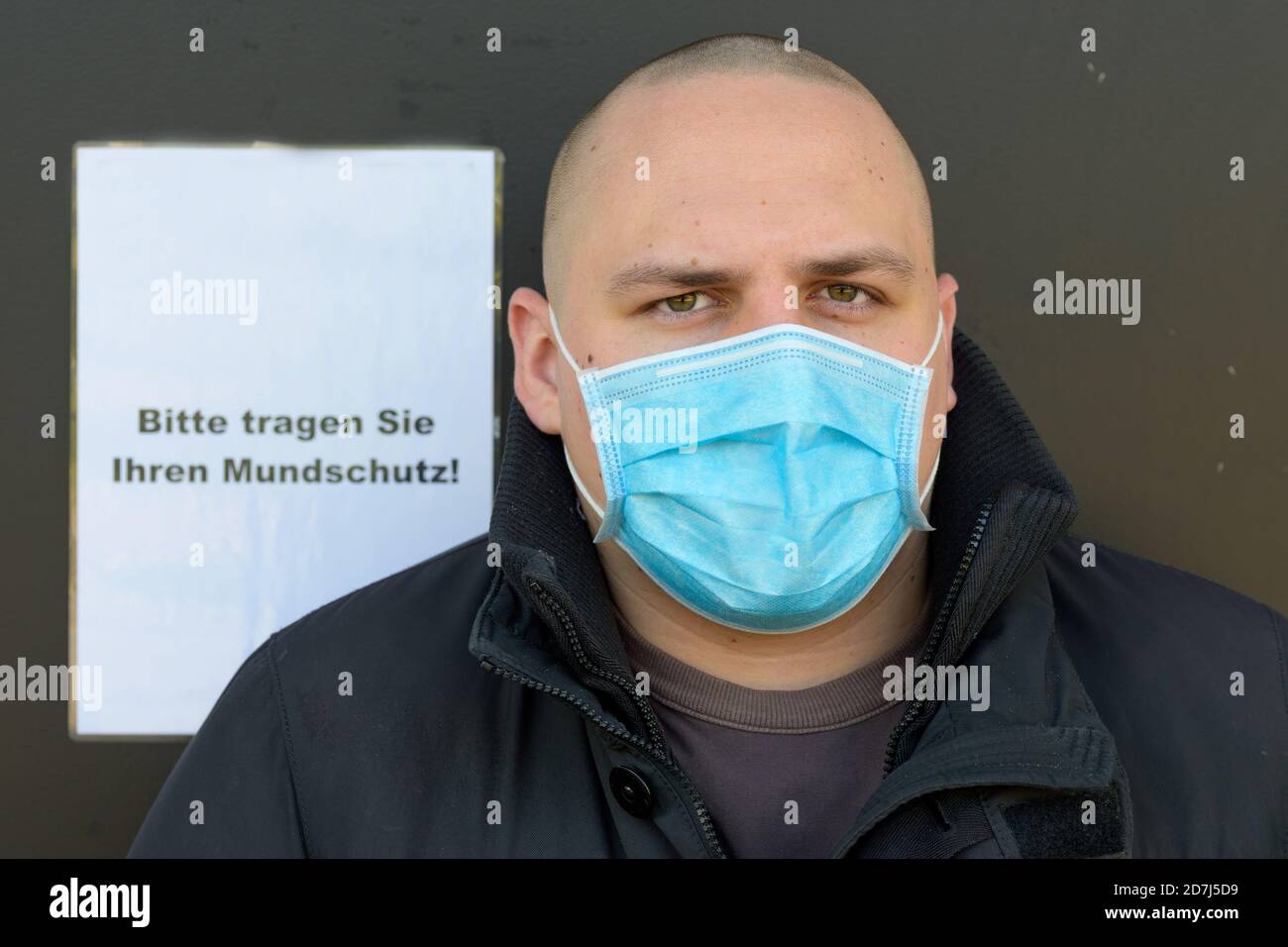 Young man wearing a face mask for infection control during the Covid-19 pandemic standing in front of a German text sign instructing people to wear th Stock Photo