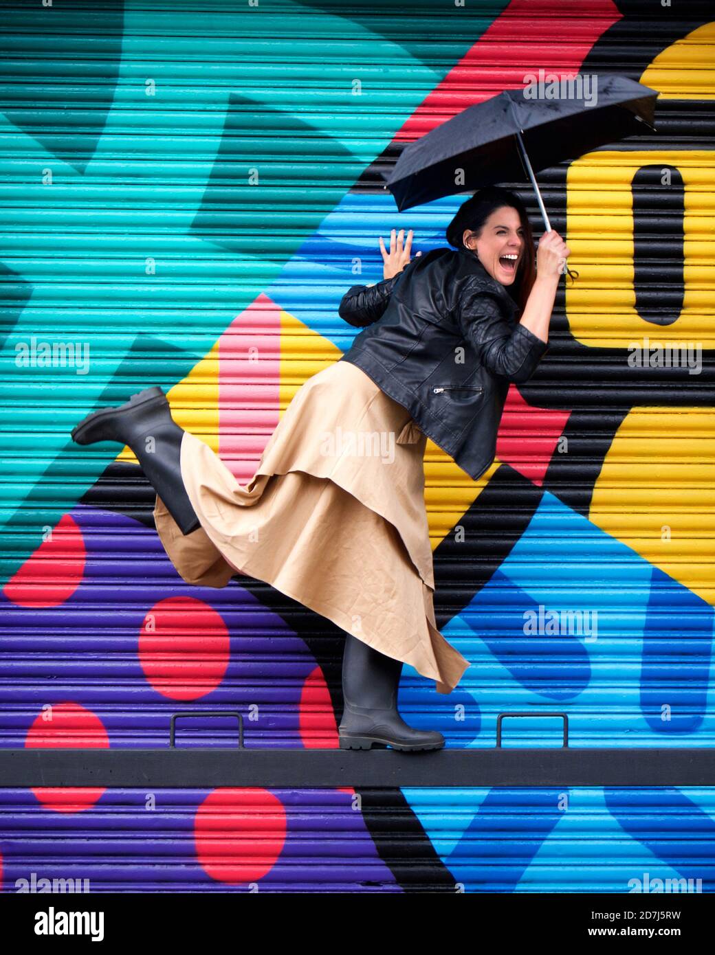 laughing woman balancing on bar in front of colourful mural Stock Photo