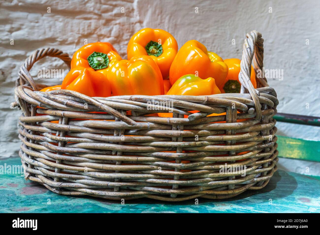 Orange bell peppers in a basket on a painted table Stock Photo