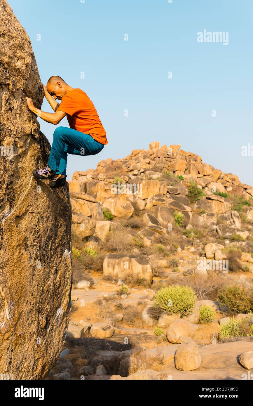 Male rock climber ascending rock wall with hill in background Stock Photo