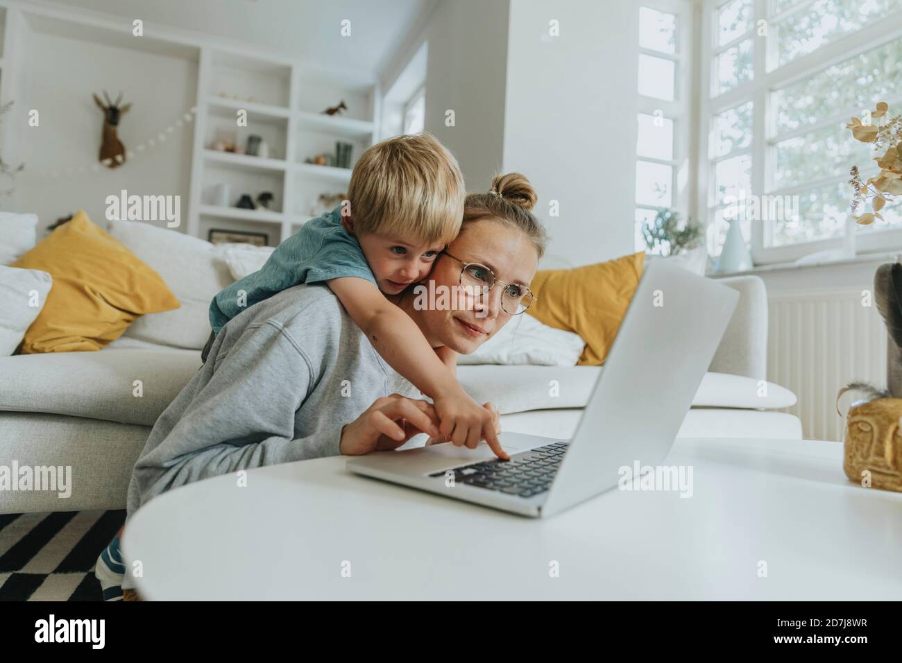 Boy doing mischief on laptop while standing behind mother at home Stock Photo
