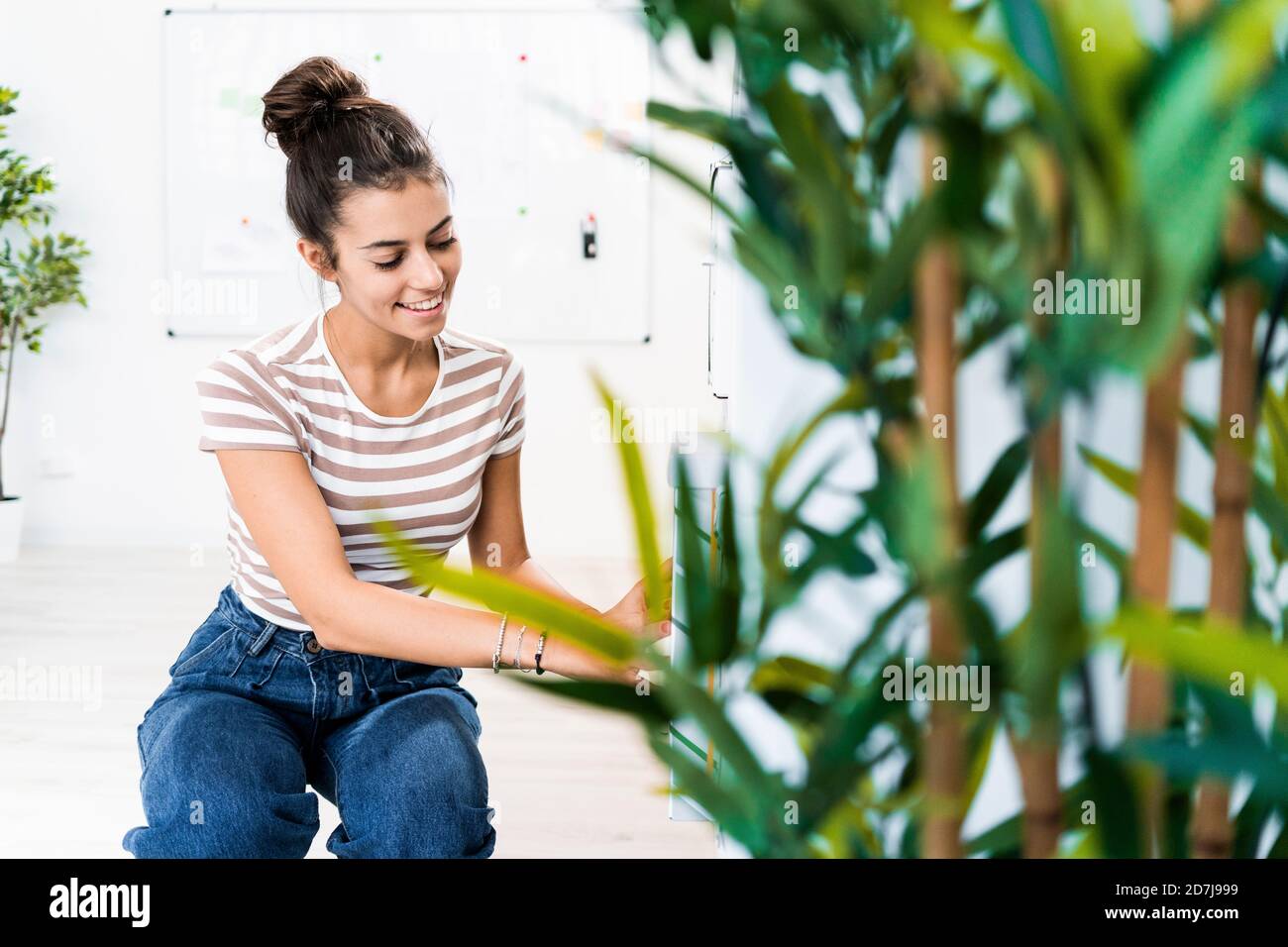 Smiling beautiful female design professional crouching by rack at creative office Stock Photo