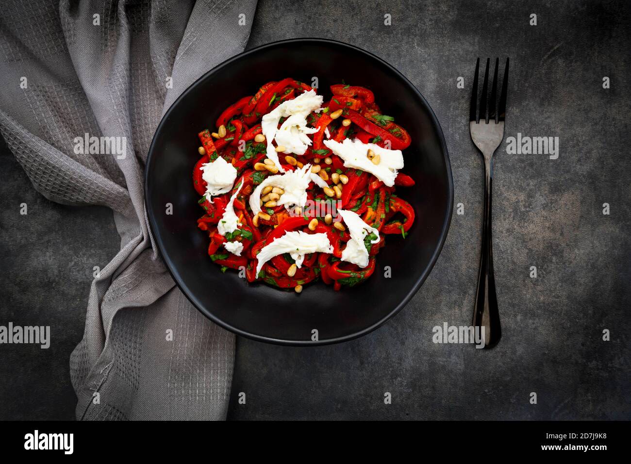 Bowl of vegetarian salad with red bell peppers, mozzarella, roasted pine nuts, parsley and chive Stock Photo