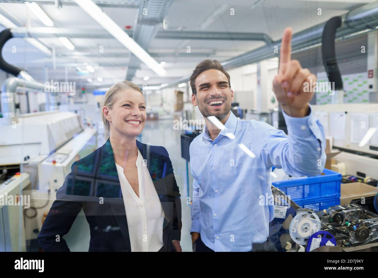 Happy young male technician pointing at graphical interface on glass in factory Stock Photo