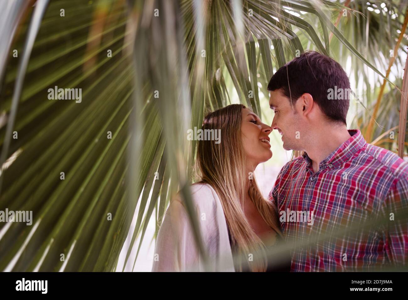 Smiling couple nuzzling nose while standing under palm leaf Stock Photo