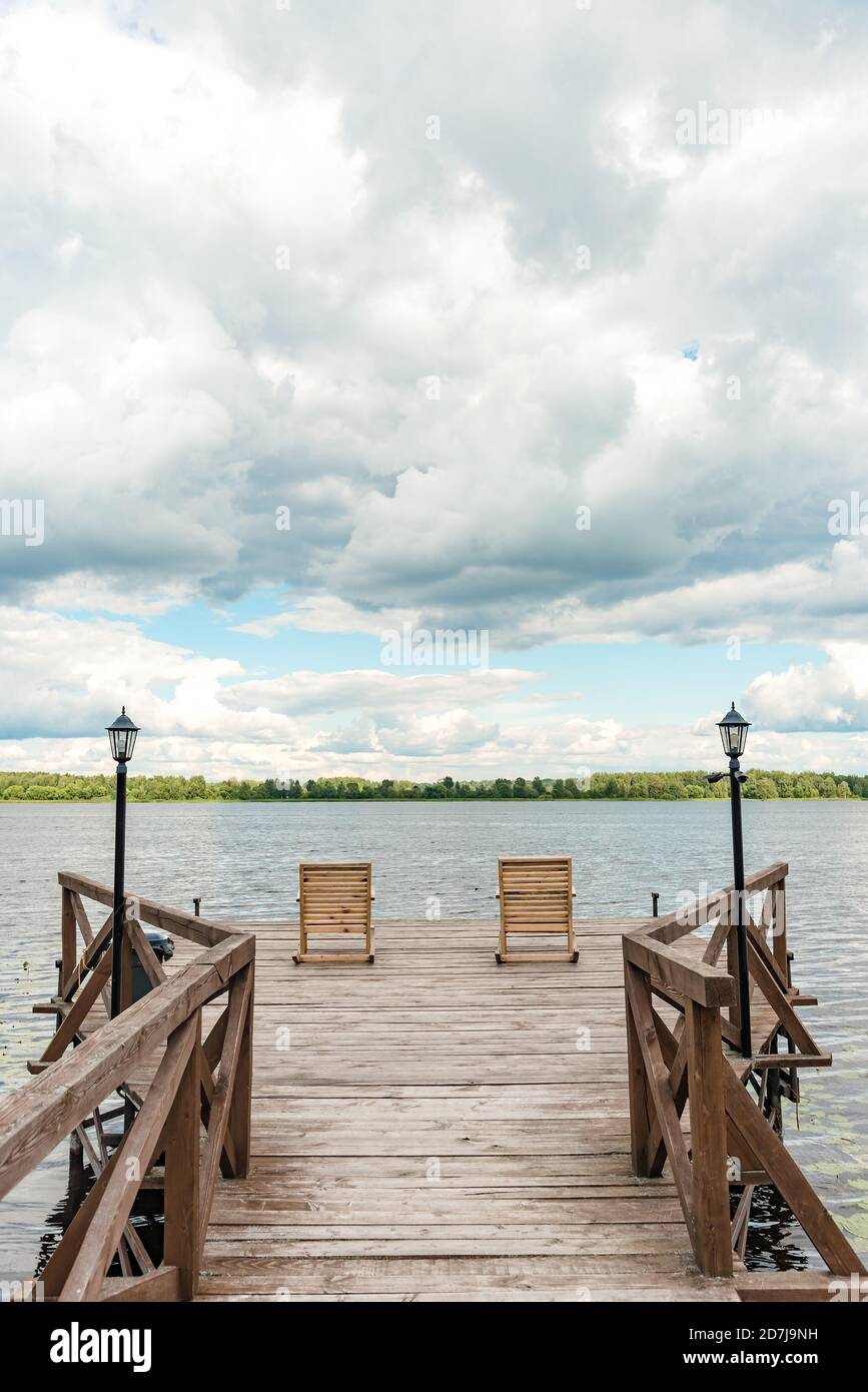 Wooden chairs on pier with streetlights near tranquil lake Stock Photo ...
