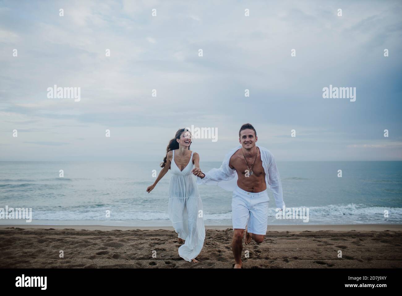 Happy couple holding hands while running on beach Stock Photo