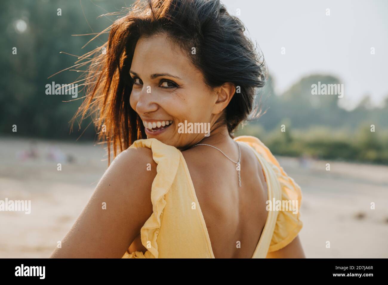 Mature woman looking over shoulder while standing at beach Stock Photo