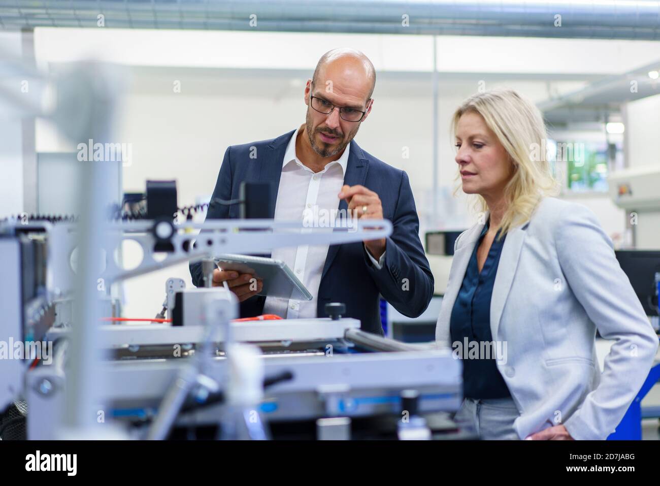 Confident businessman and businesswoman discussing while looking at machinery in factory Stock Photo