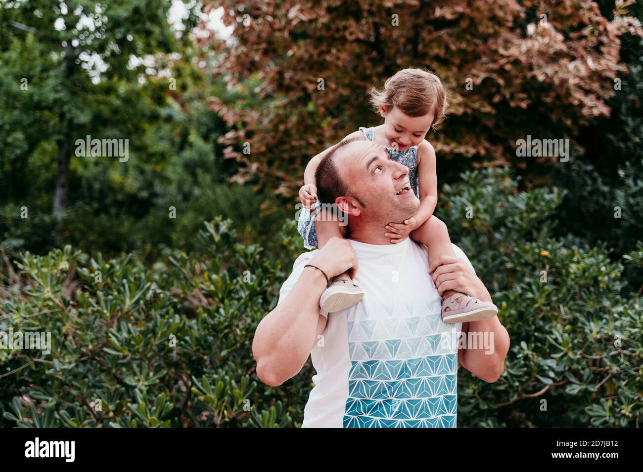 Father carrying daughter on shoulder while standing in park Stock Photo ...