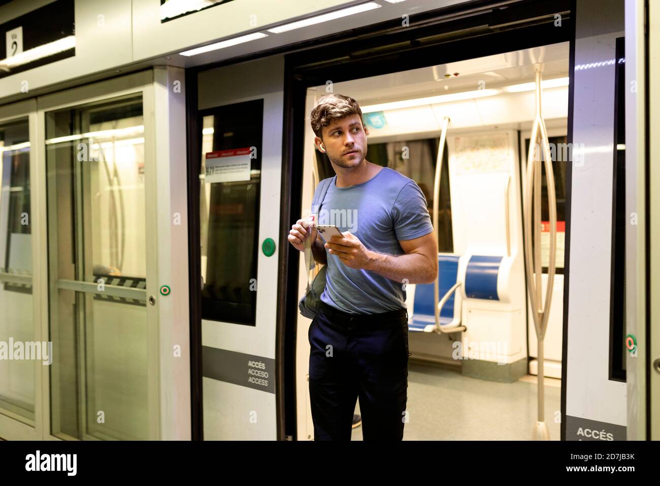 Handsome young male commuter looking away while disembarking from subway train at station Stock Photo