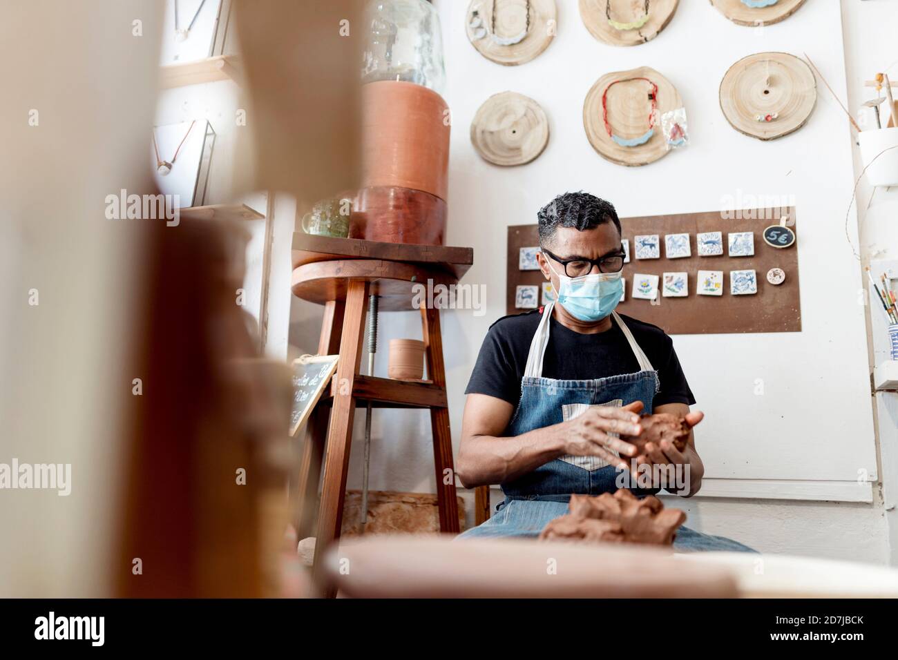 Potter wearing mask holding clay while sitting in workshop Stock Photo