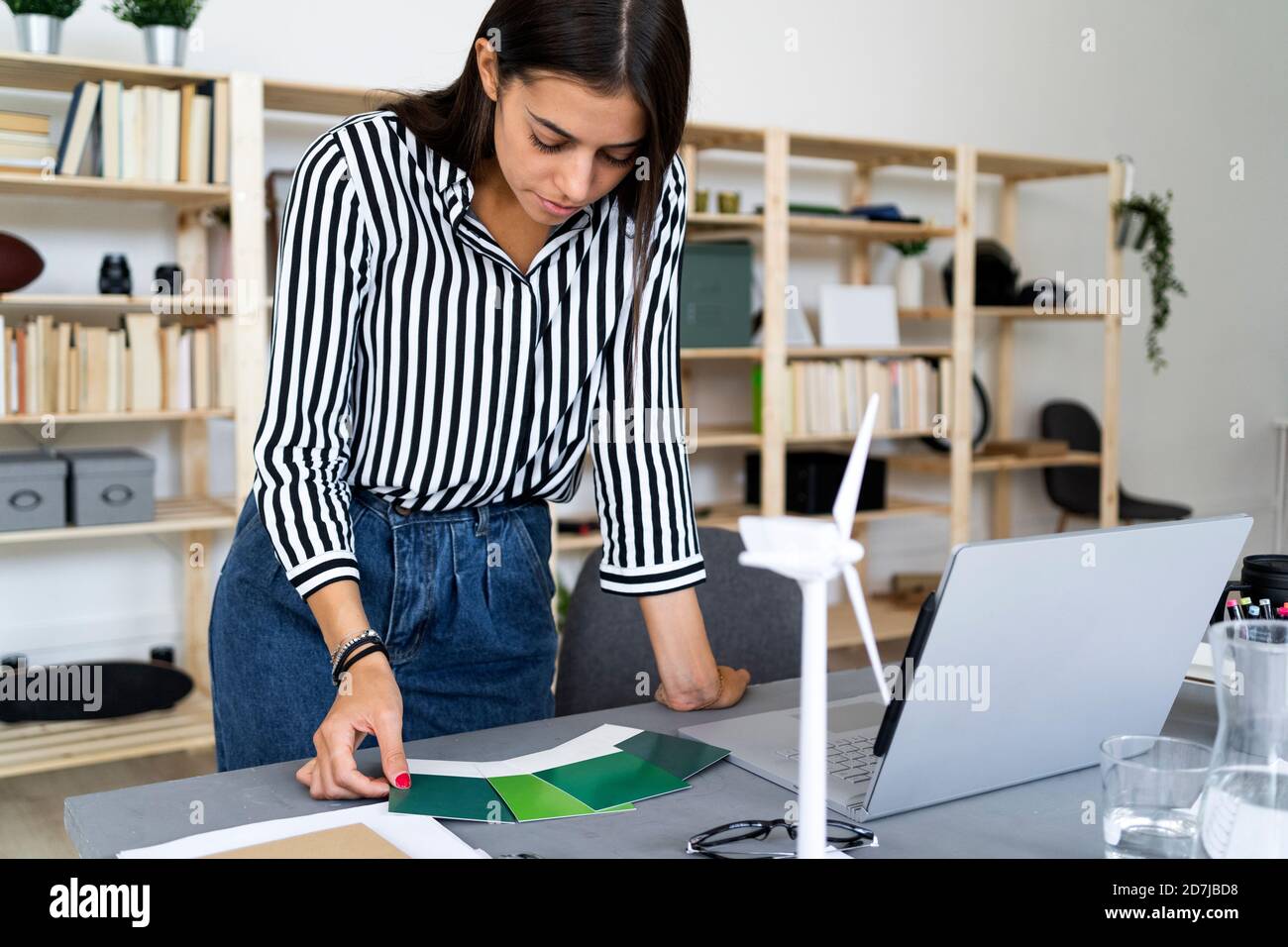 Young female architect making decision in choosing color shade from swatches at desk in office Stock Photo