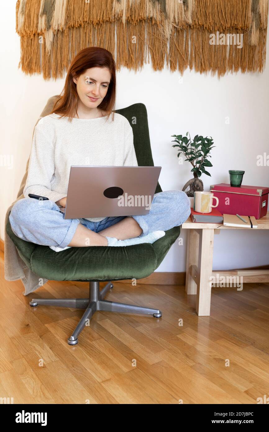 Young woman sitting on chair while working on laptop at home Stock ...