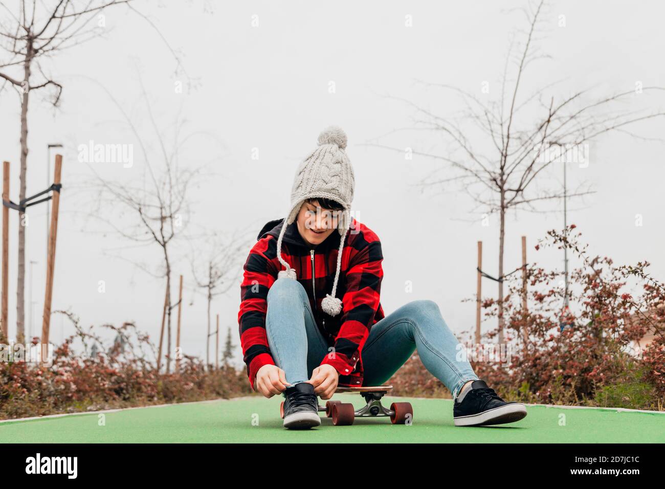 Young woman tying shoelace while sitting on skateboard Stock Photo