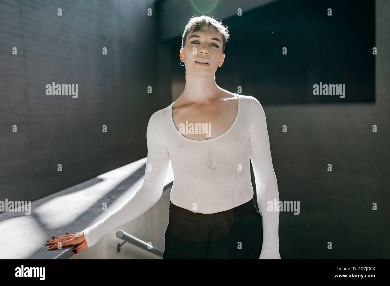 Non-binary young man wearing white leotard standing in basement Stock Photo