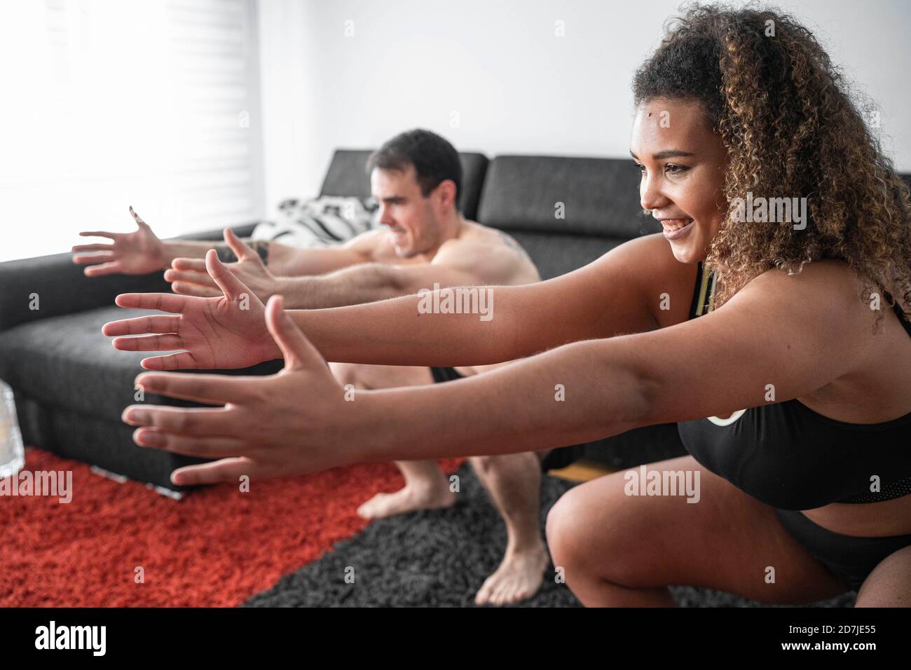 Couple crouching while exercising together at home Stock Photo
