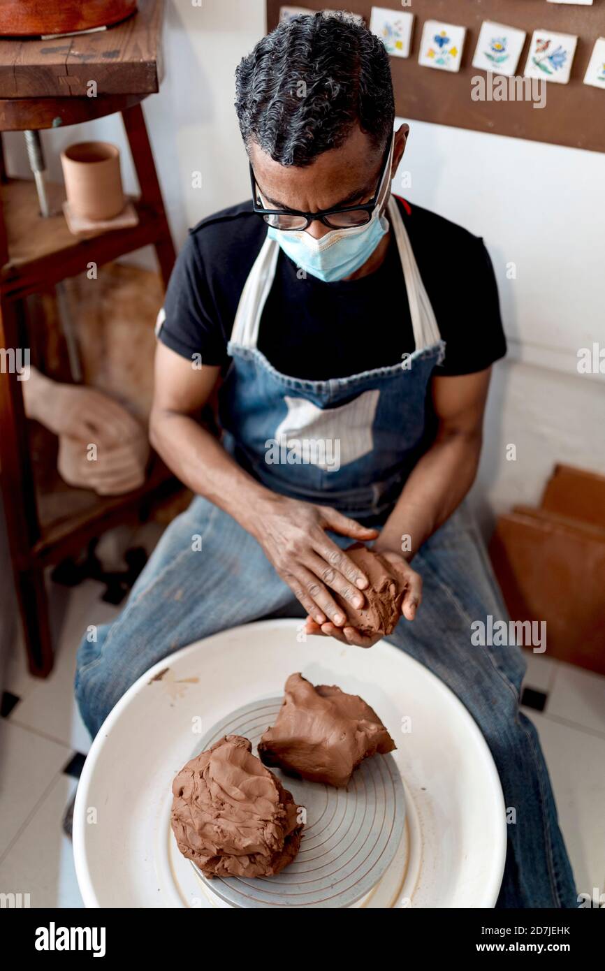 Male potter wearing mask holding clay while sitting in workshop Stock Photo
