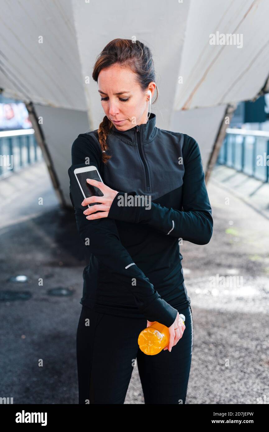 Female athlete using smart phone over arm band while standing on footpath Stock Photo