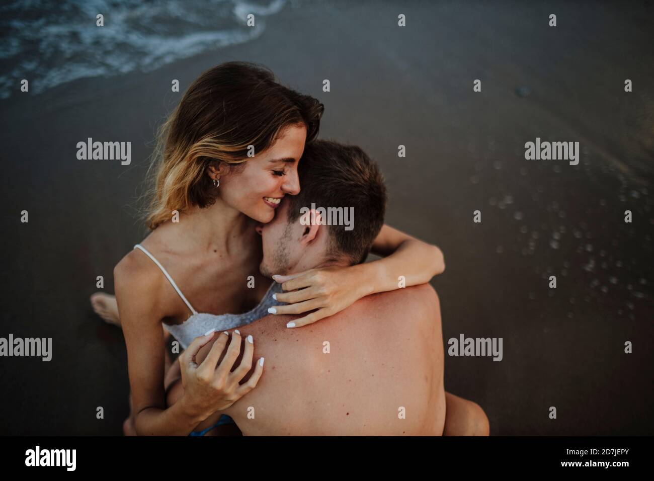 Man embracing woman while sitting on beach Stock Photo