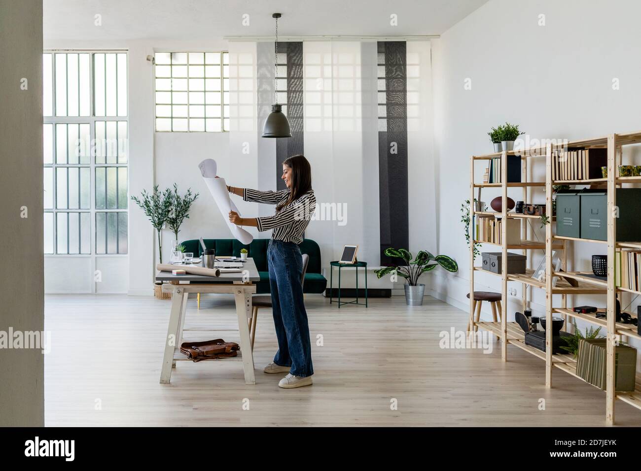 Smiling young female architect looking at blueprint while standing ...