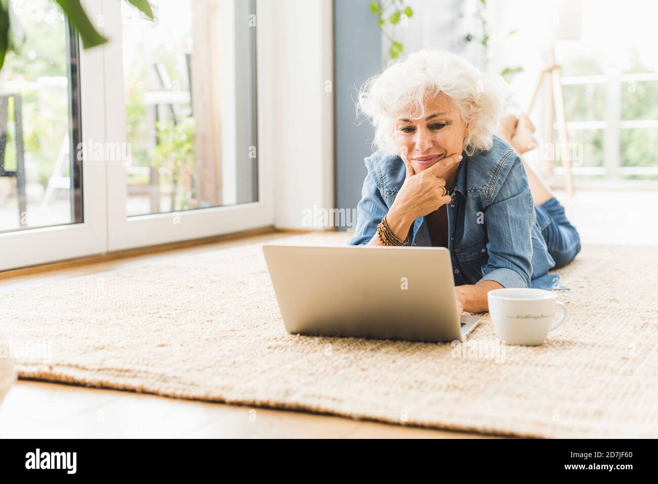 Mature woman lying on front while working on laptop at home Stock Photo