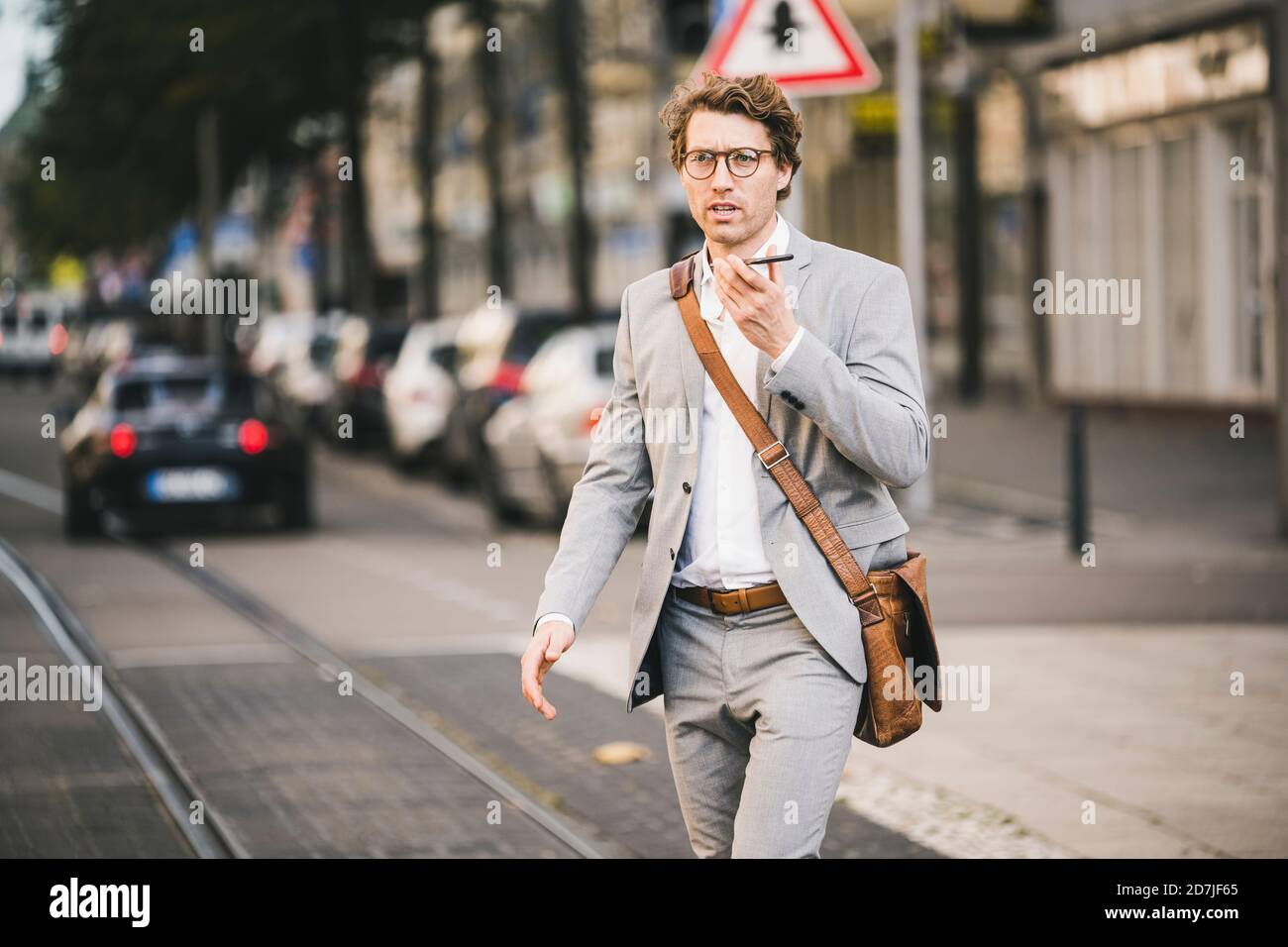 Man wearing eyeglasses talking on mobile phone while walking at tramway in city Stock Photo