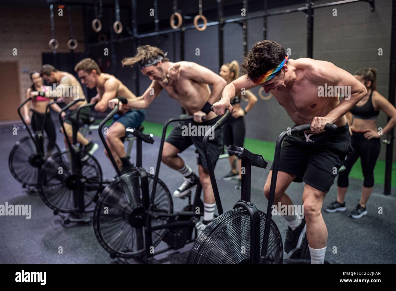 Athletes cycling on exercise bike with women standing in background at gym Stock Photo