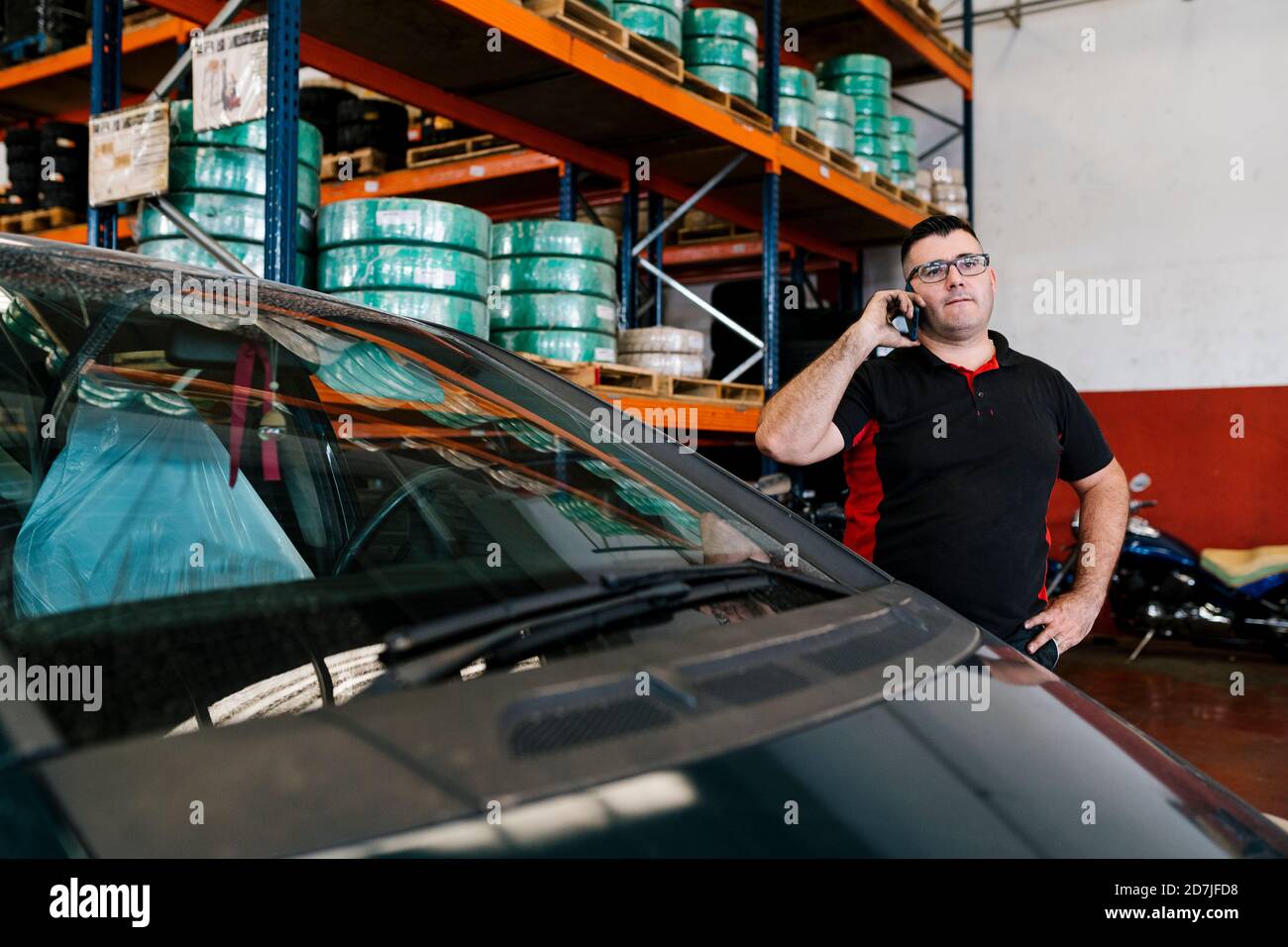 Mechanic talking over mobile phone while standing by car in auto repair shop Stock Photo