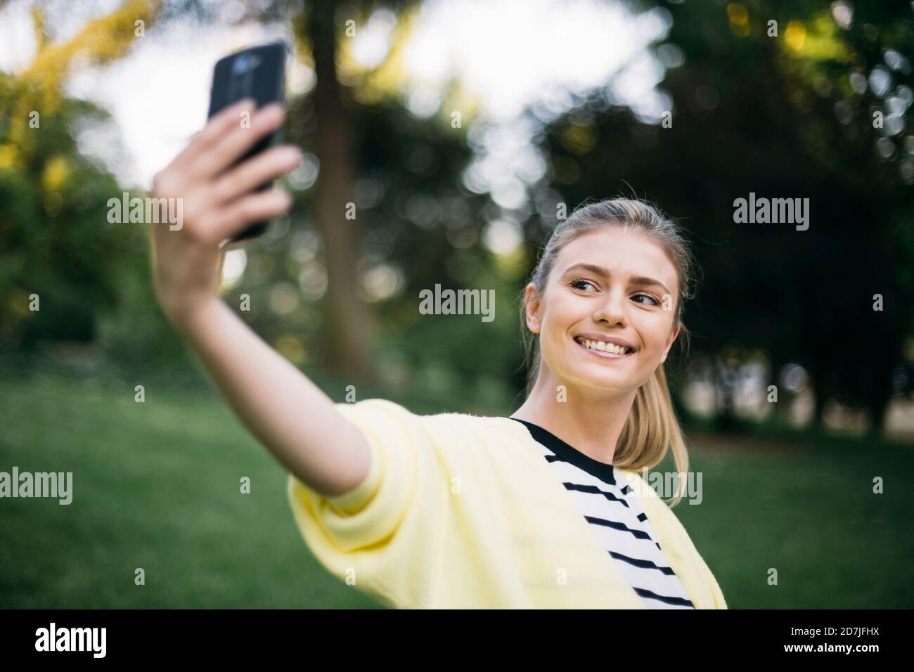 Woman smiling while taking selfie in public park Stock Photo - Alamy