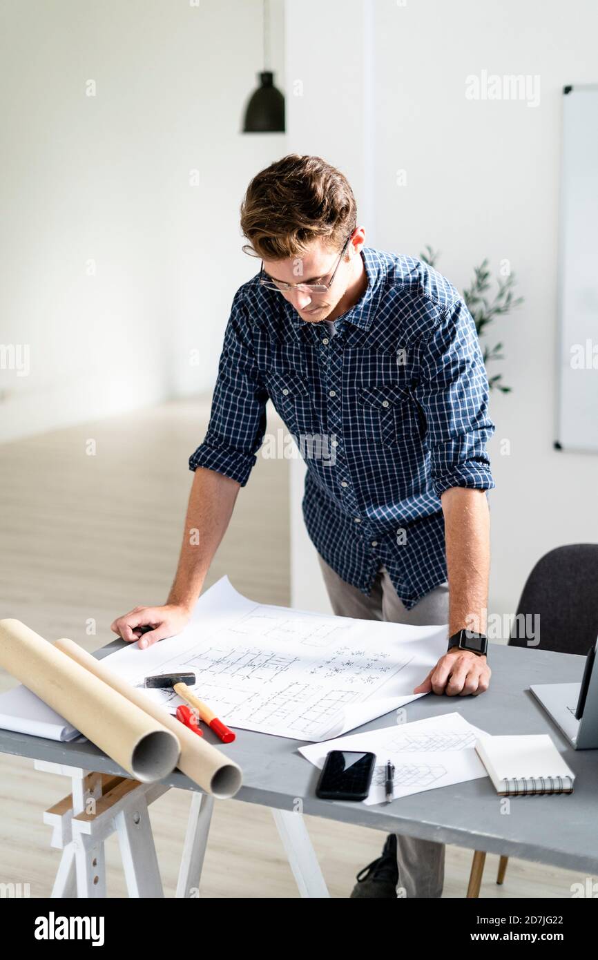 Architect analyzing blueprint while standing by desk at office Stock Photo