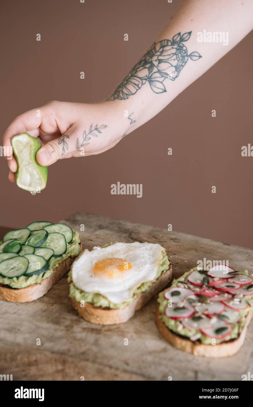 Woman squeezing lime on bread garnished with vegetable and guacamole on serving dish at kitchen Stock Photo