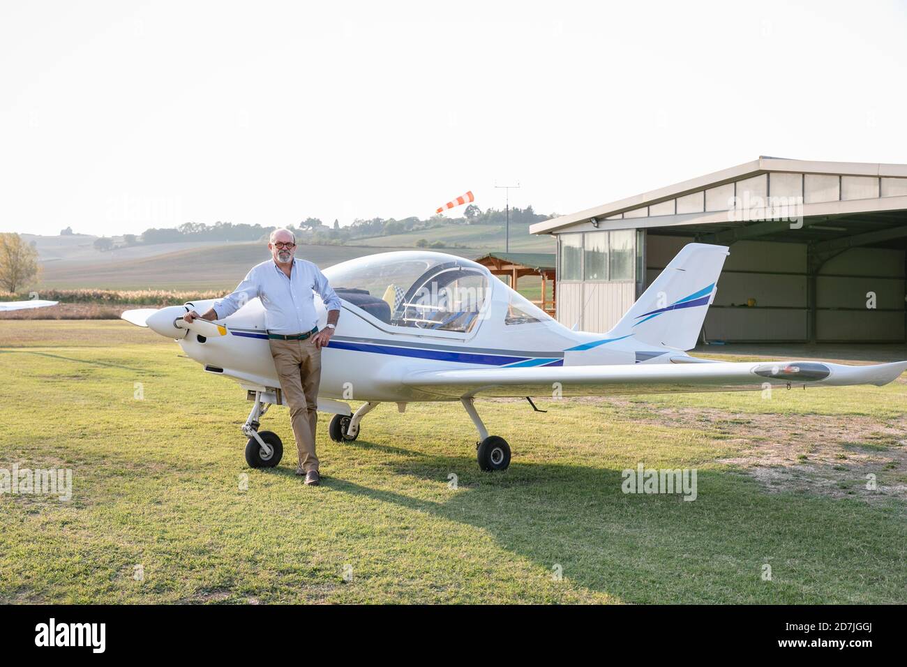 Senior man with hand on hip standing against airplane at airfield Stock Photo