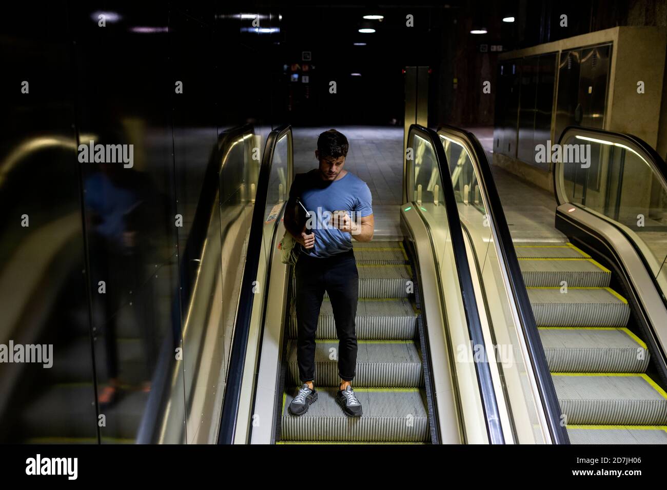 Young man using smart phone while holding digital tablet on escalator at subway Stock Photo