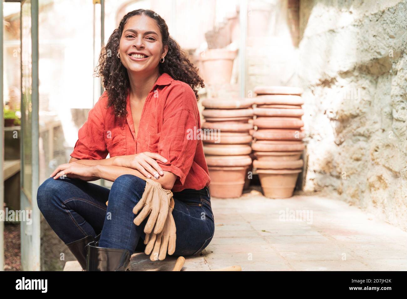 Smiling mature woman with gardening glove sitting in garden shed Stock Photo