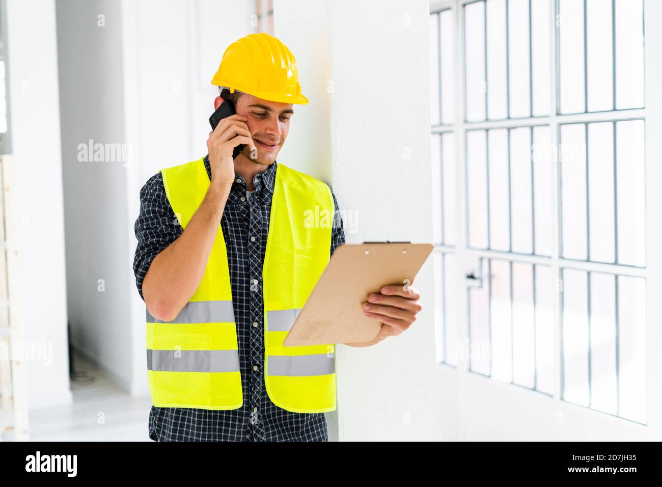 Smiling architect holding notepad while talking on mobile phone at office under construction Stock Photo